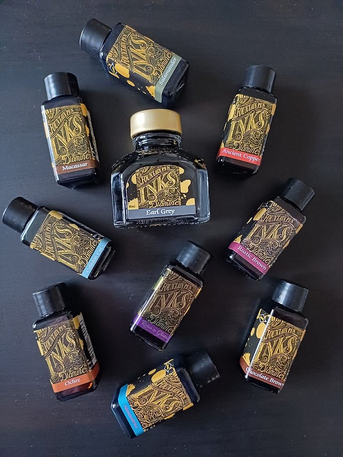Ten ink bottles spread out on a black table top.