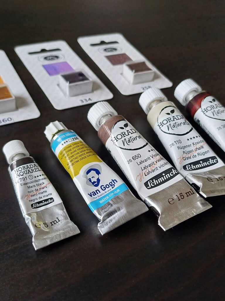 Five paint tubes and three half pans in browns, greys, purple, yellow-green, black and red.