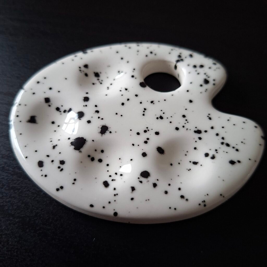 An artist palette shaped small ceramic palette in white with black speckles.