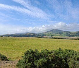 Maughold Countryside scene with fields and hills. The sky is blue with a high layer of thin, broken cloud.