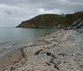 Port e Vullen A cloudy scene of a sandy cove with pebbles.