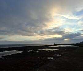 Castletown Beach An orange, yellow and blue sky with clouds over a darkened beach and small town.